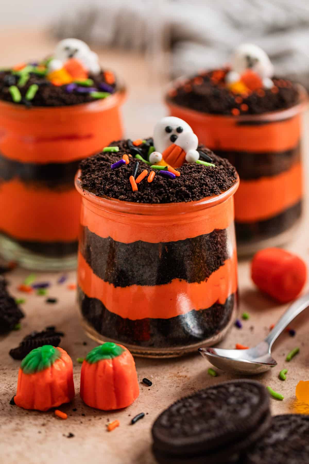 Orange and black layered pudding and crushed Oreos in glass jars with Halloween themed sprinkles and candy.