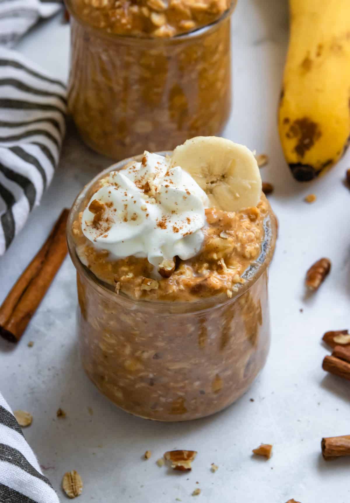 Pumpkin banana overnight oats in jars with banana slices and whipped cream.
