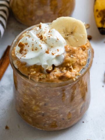 Pumpkin banana overnight oats in jar with whipped cream and cinnamon.