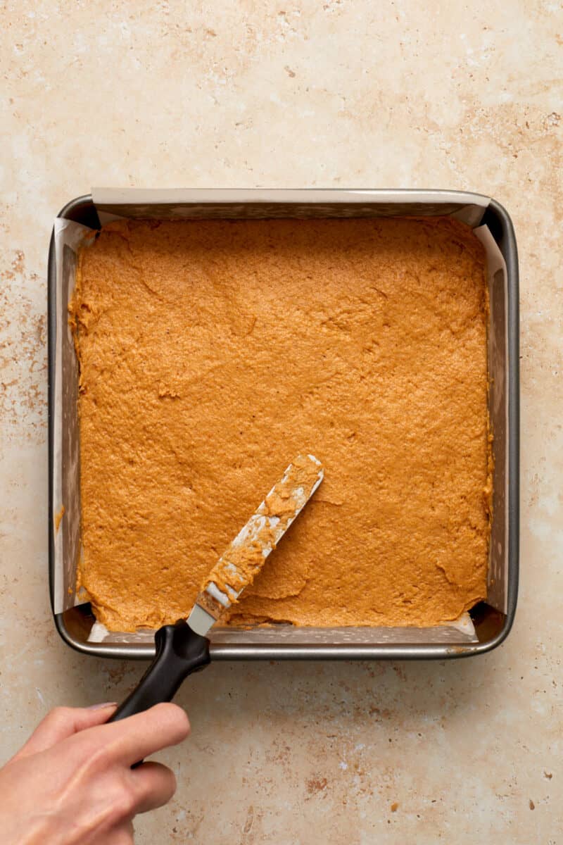 Pumpkin coffee cake in parchment lined baking pan with spatula spreading over top.