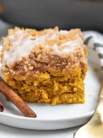 Slice of cinnamon streusel topped coffee cake with fork and cinnamon sticks on white plate.