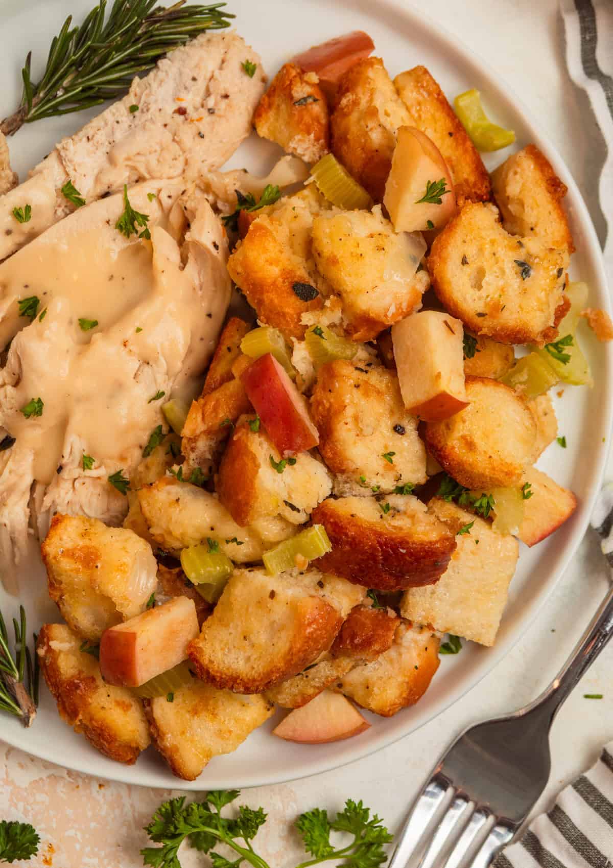 Apple stuffing on white plate with turkey and gravy over top.