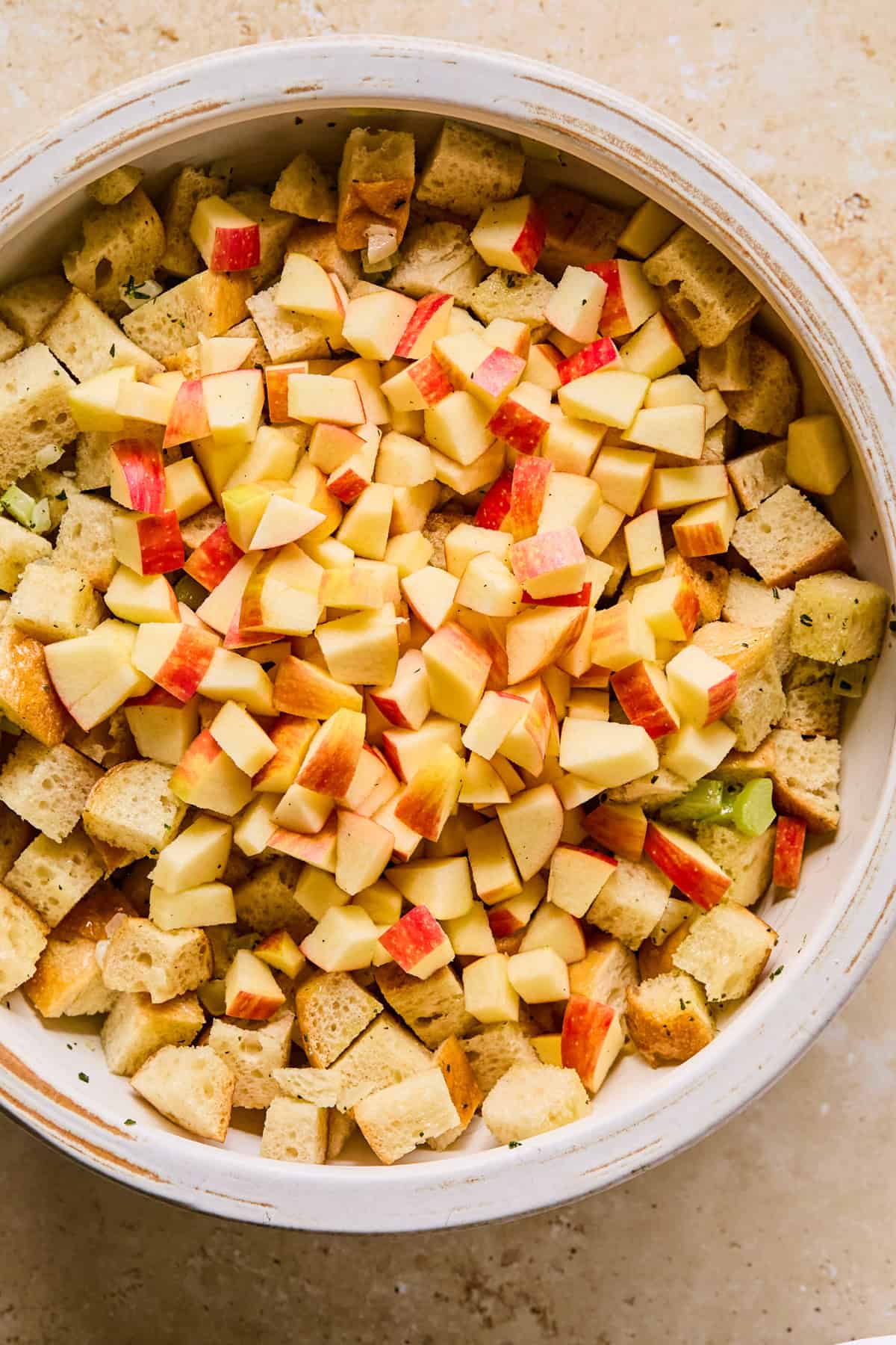 Celery and onion mixture added to mixing bowl with chopped apples added on top.