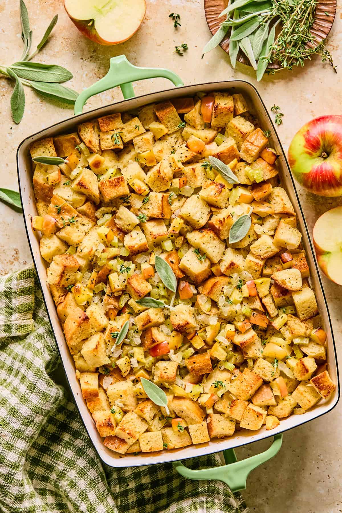 Apple stuffing in baking pan with chopped herbs and fresh sage on top.