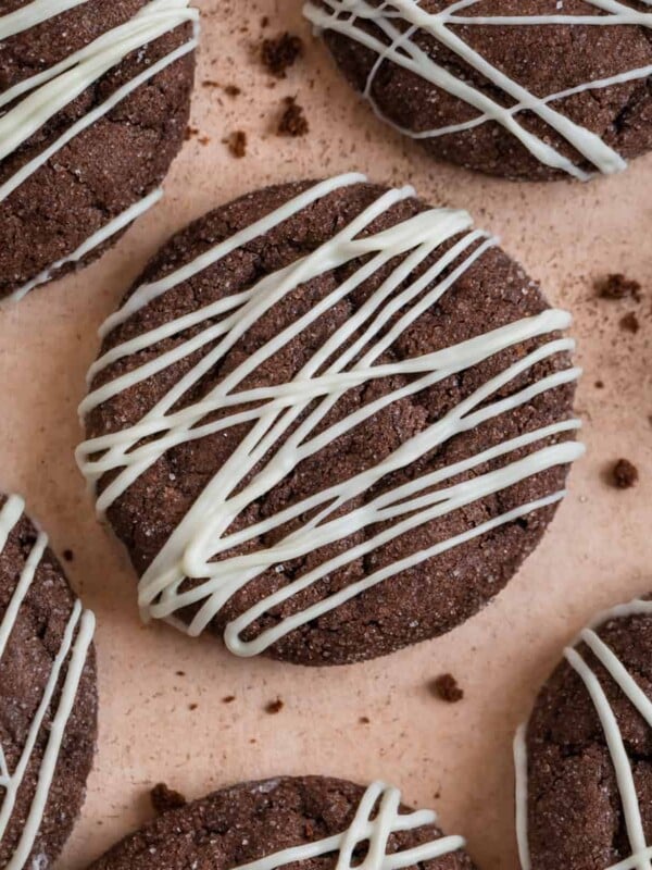 Chocolate cake mix cookies with white chocolate drizzle surrounded by cookie crumbs.