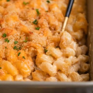 Dish with gruyere mac and cheese baked in baking pan with serving spoon scooping up a serving.