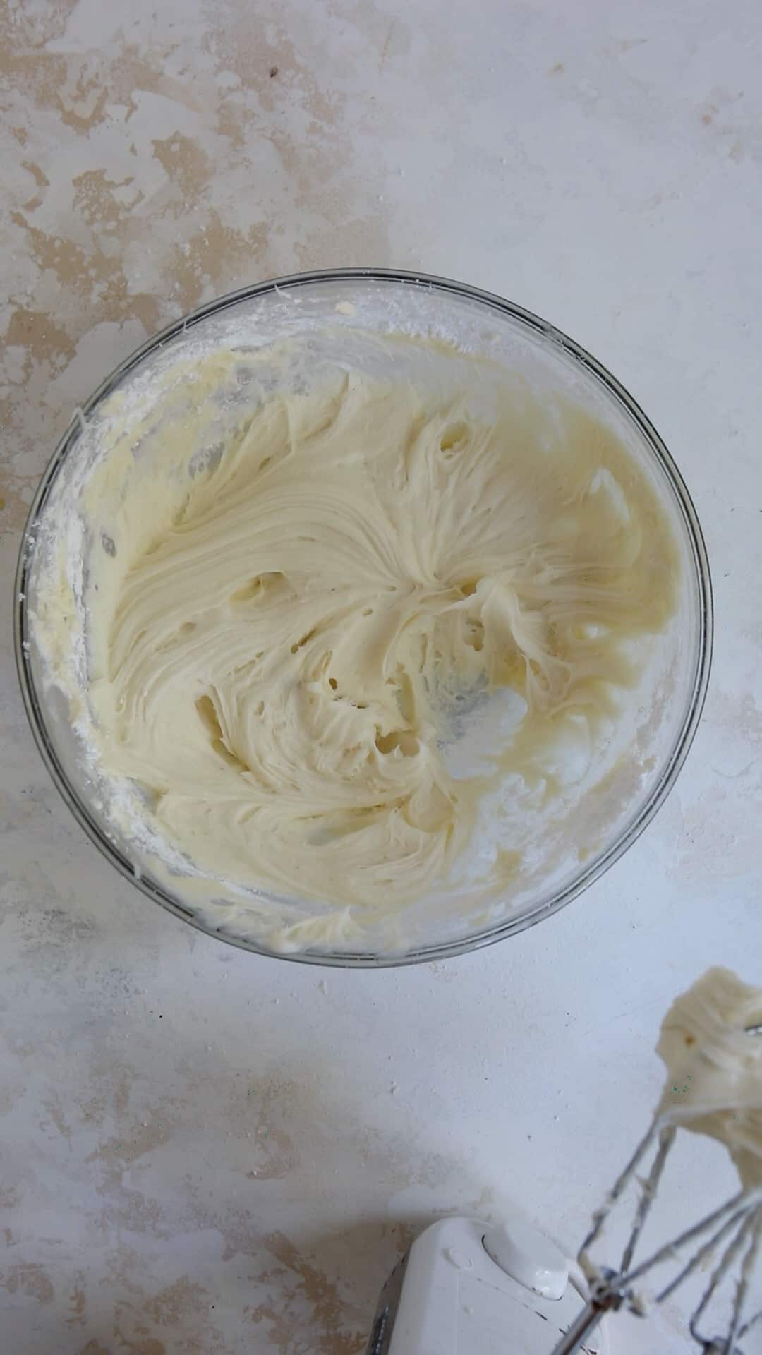 Cream cheese icing in mixing bowl with electric mixer beside it.