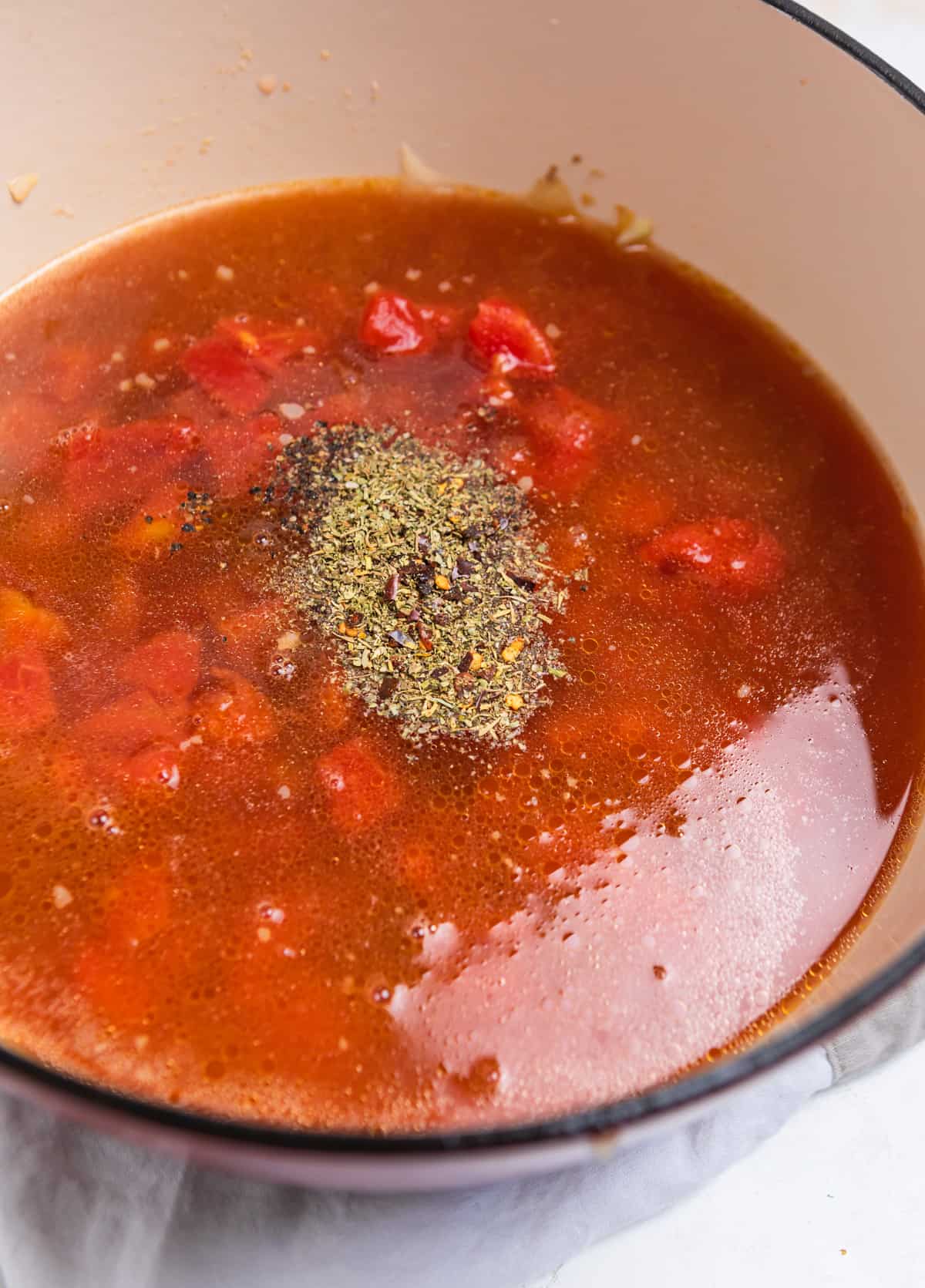 Pot with broth, tomatoes and seasonings added over top.