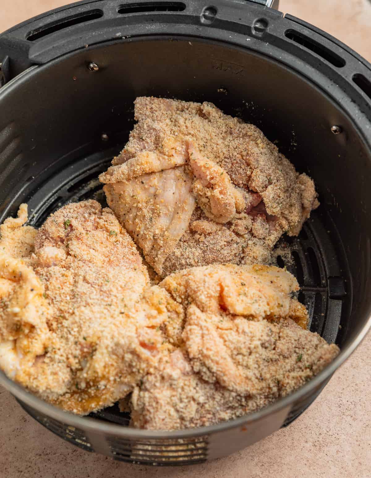 Air fryer basket with breaded chicken thighs.
