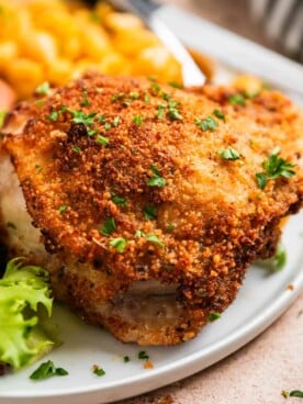 Crispy breaded air fryer parmesan chicken thigh on white plate topped with parsley.