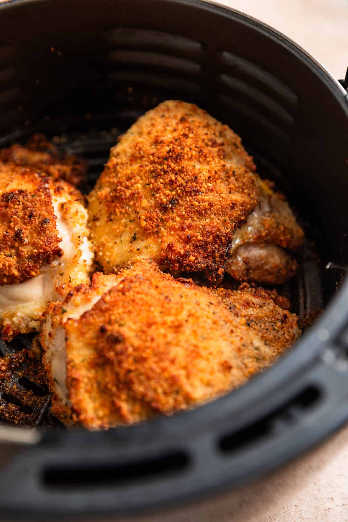 Air fryer basket with crispy breaded parmesan chicken thighs.