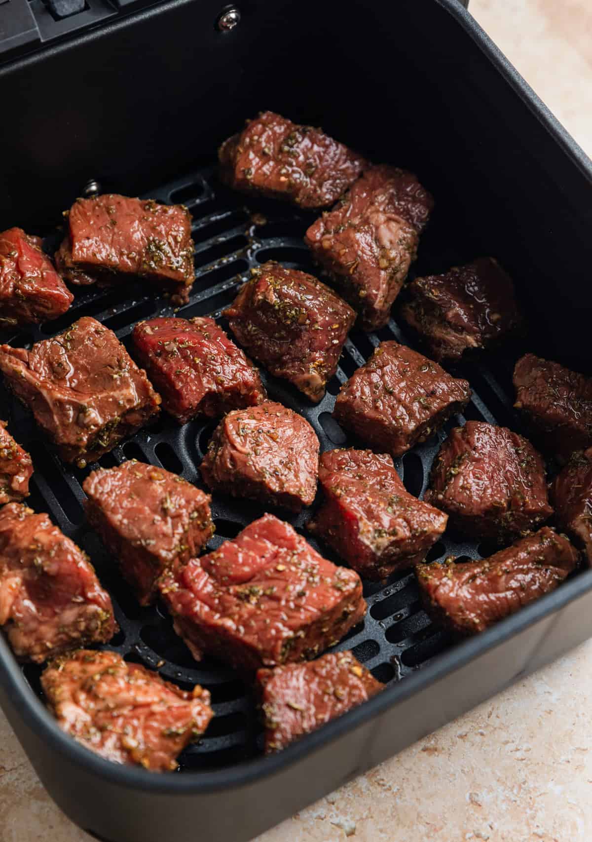 Marinaded sirloin steak bites in air fryer basket before cooking.