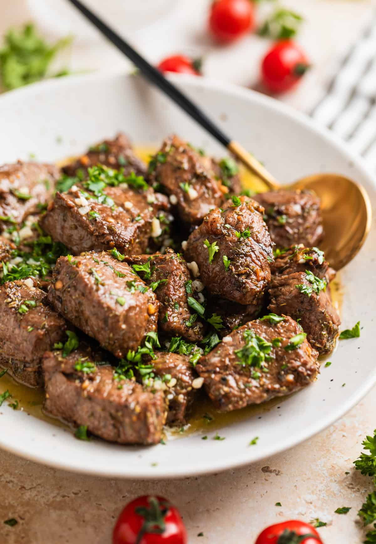 White serving dish with air fryer steak bites in lemon garlic butter sauce topped with chopped parsley.