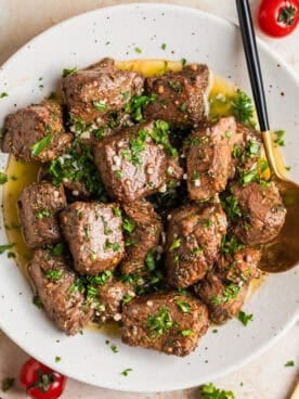 White plate with air fryer steak bites in lemon garlic butter sauce with fresh parsley over top.