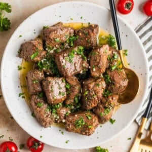 White plate with air fryer steak bites in lemon garlic butter sauce with fresh parsley over top.