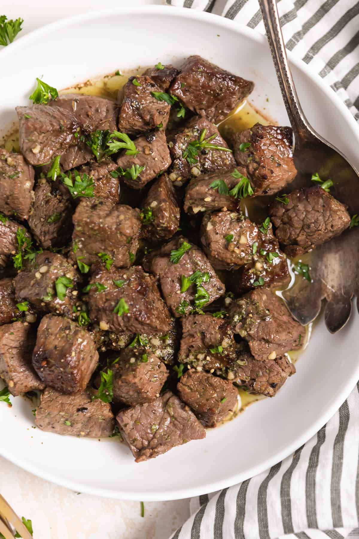 Overhead view of white dish with air fryer steak bites in lemon garlic butter sauce with fresh parsley over top.