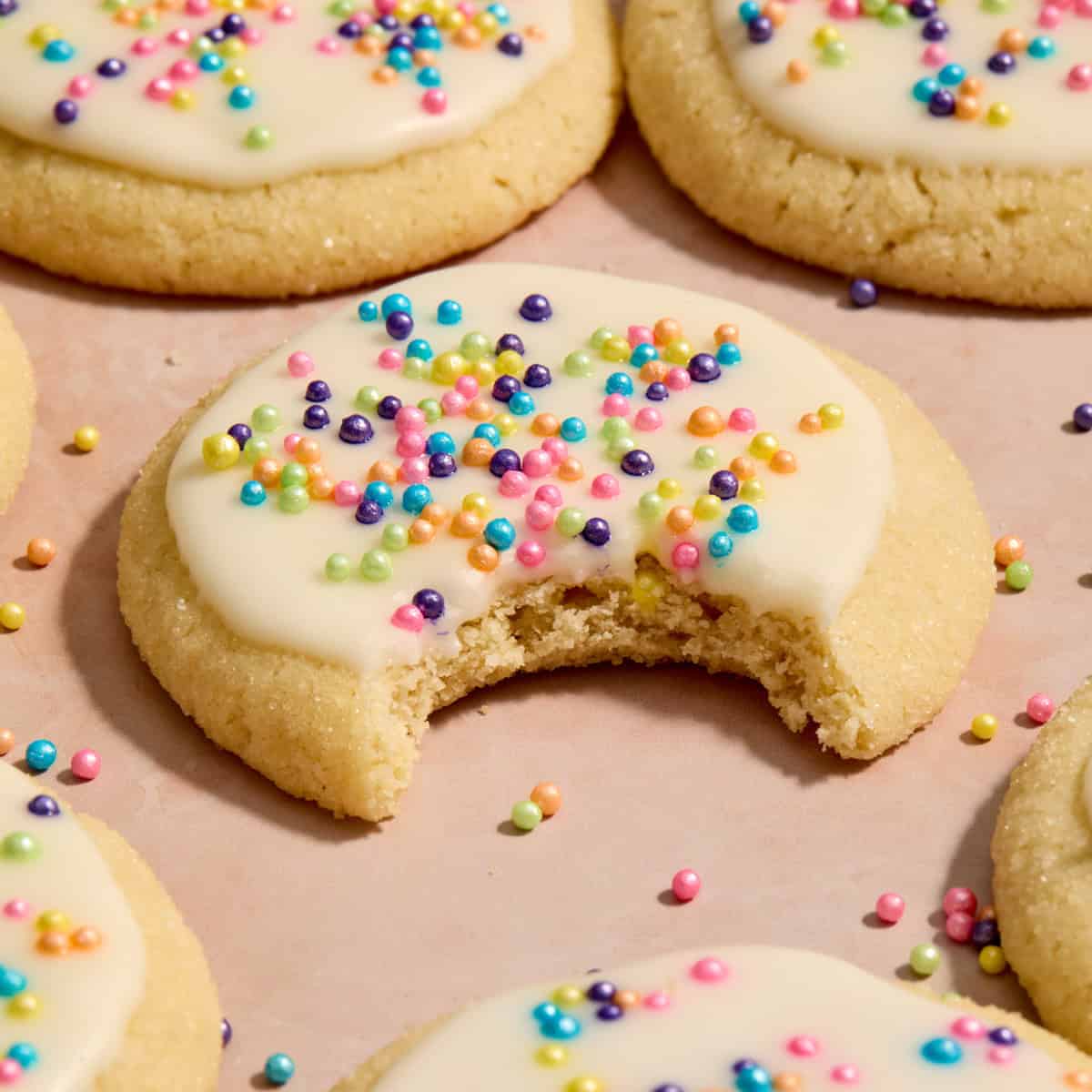 Eggless sugar cookies on surface with bite taken out of cookie.