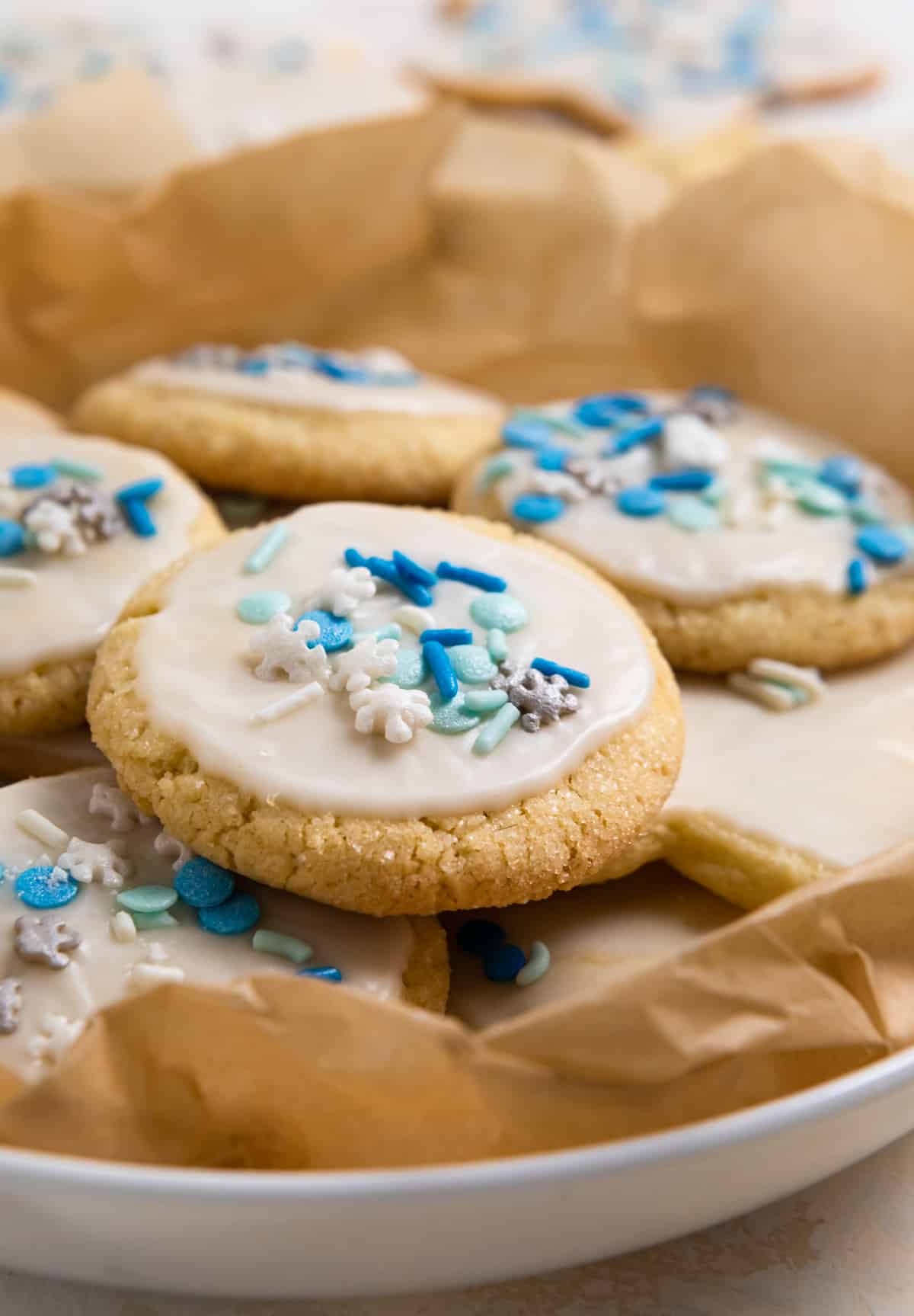 Plate of eggless sugar cookies with white glaze and blue sprinkles in parchment.