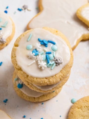Stack of egg free sugar cookies with white icing and blue and white sprinkles.