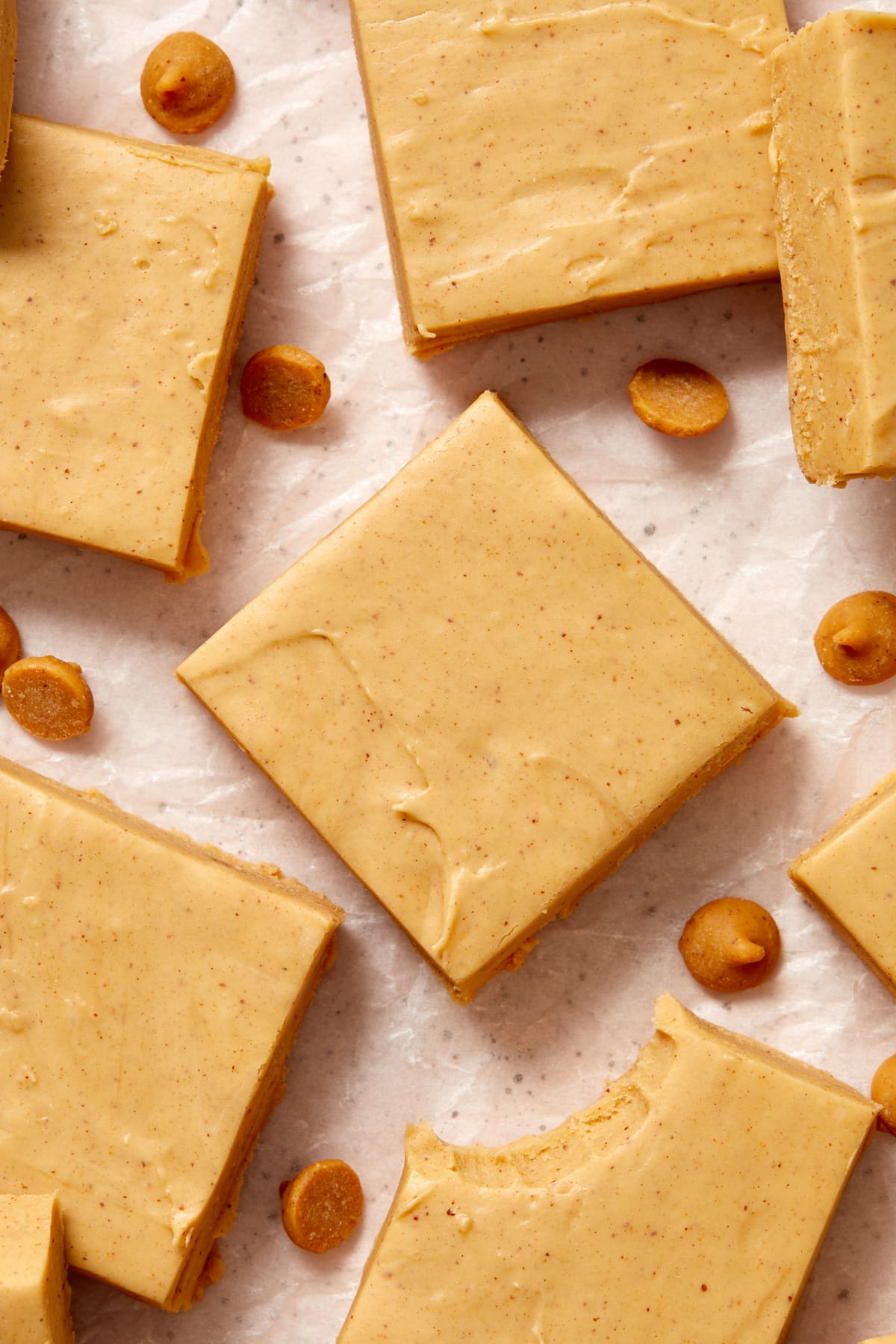 Squares of peanut butter fudge on wax paper with peanut butter chips.