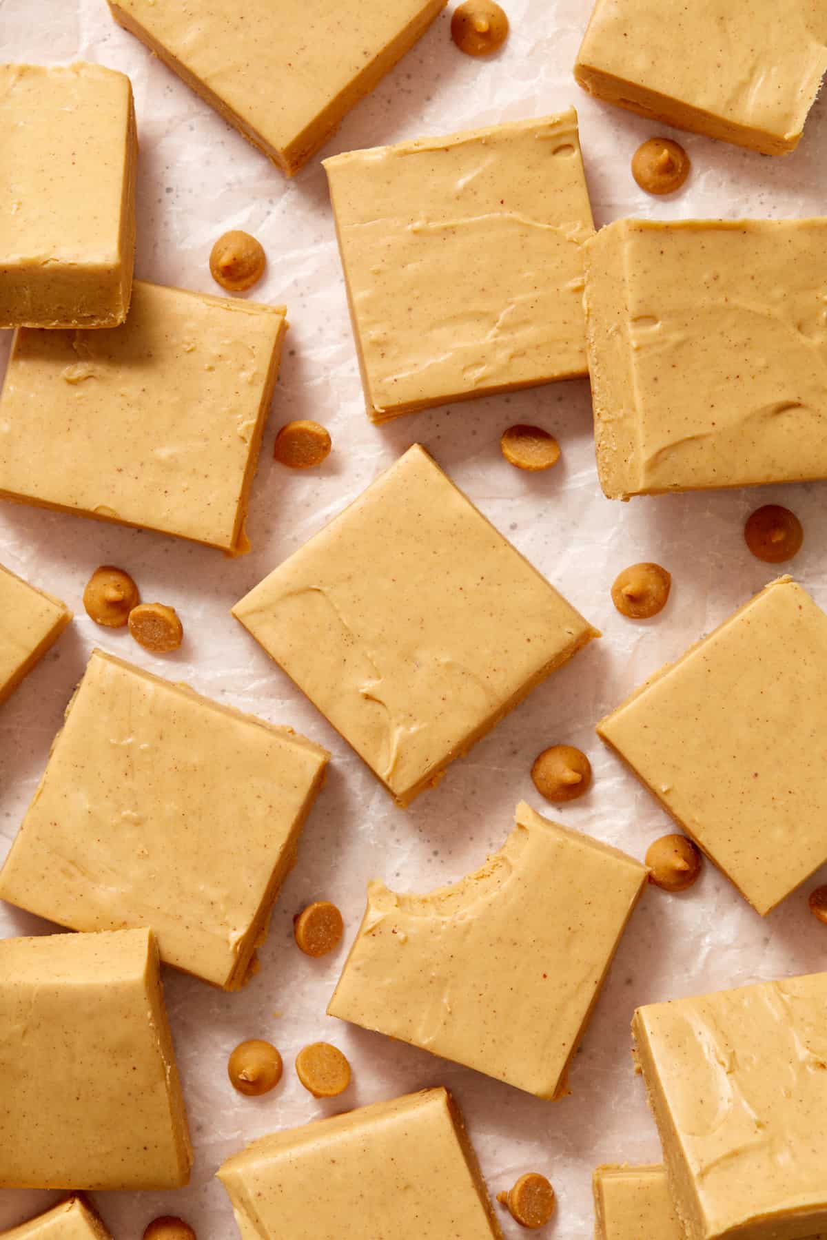 Peanut butter fudge cut in squares arranged on surface with peanut butter chips.