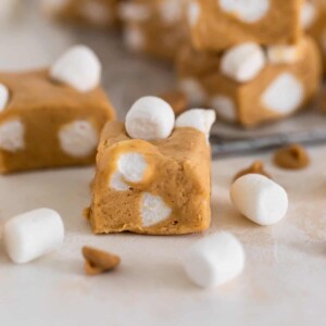 Piece of marshmallow peanut butter fudge with peanut butter chips and marshmallows surrounding.