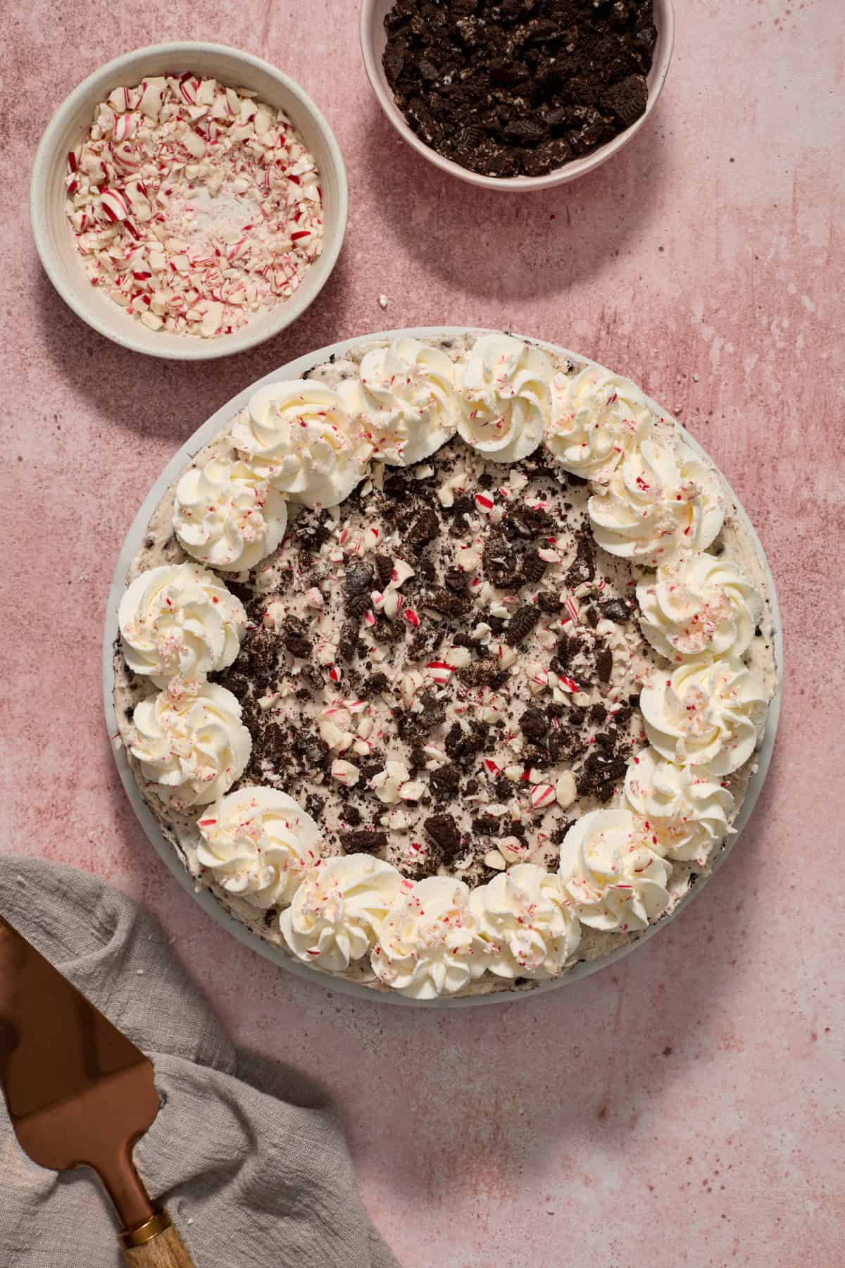 Ready to serve Oreo peppermint cheesecake topped with whipped cream edges and extra candy canes and cookies sprinkled over top.