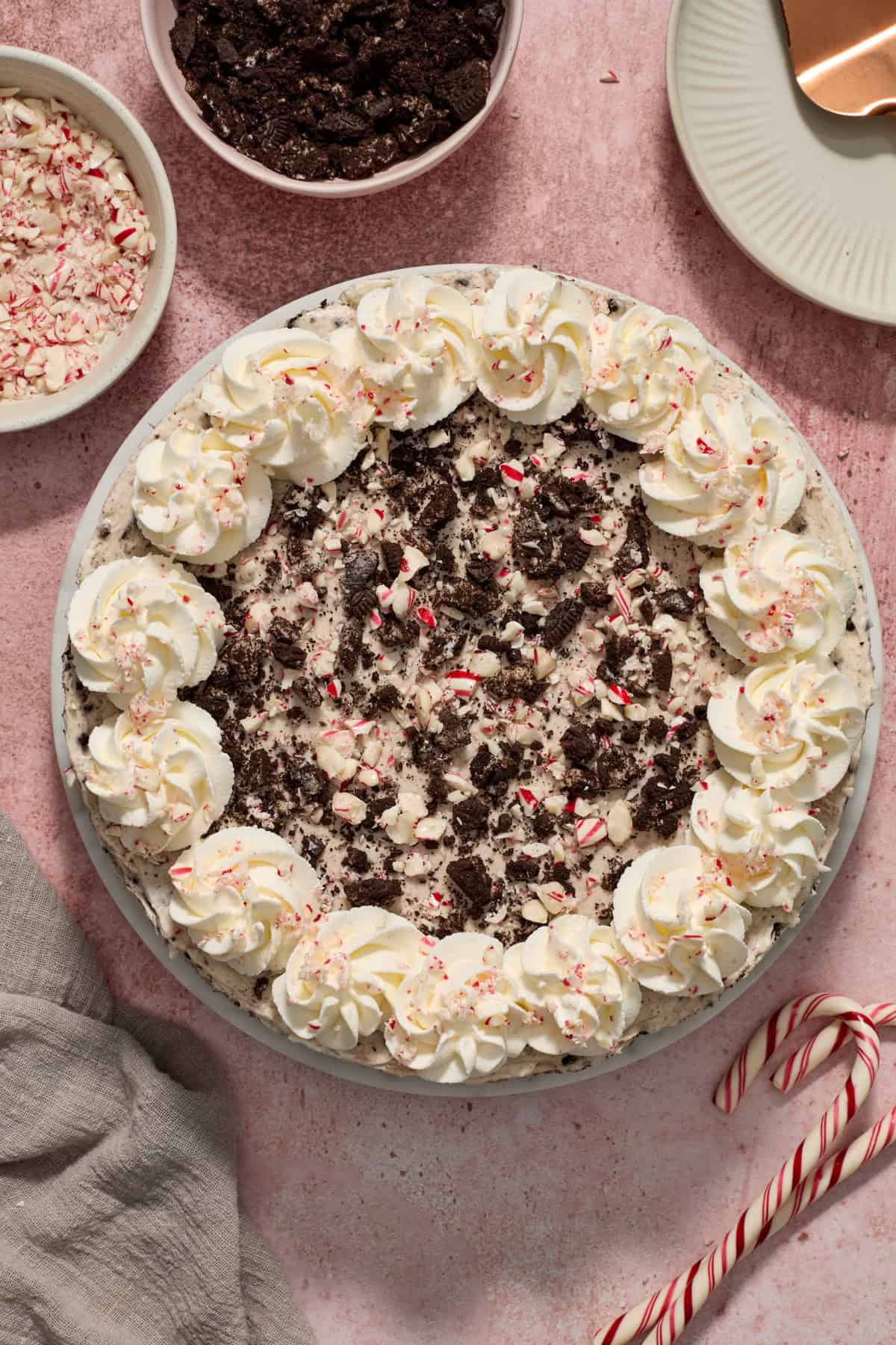 No bake peppermint Oreo cheesecake with whipped cream around the edges and extra crushed cookies and candy canes on top.