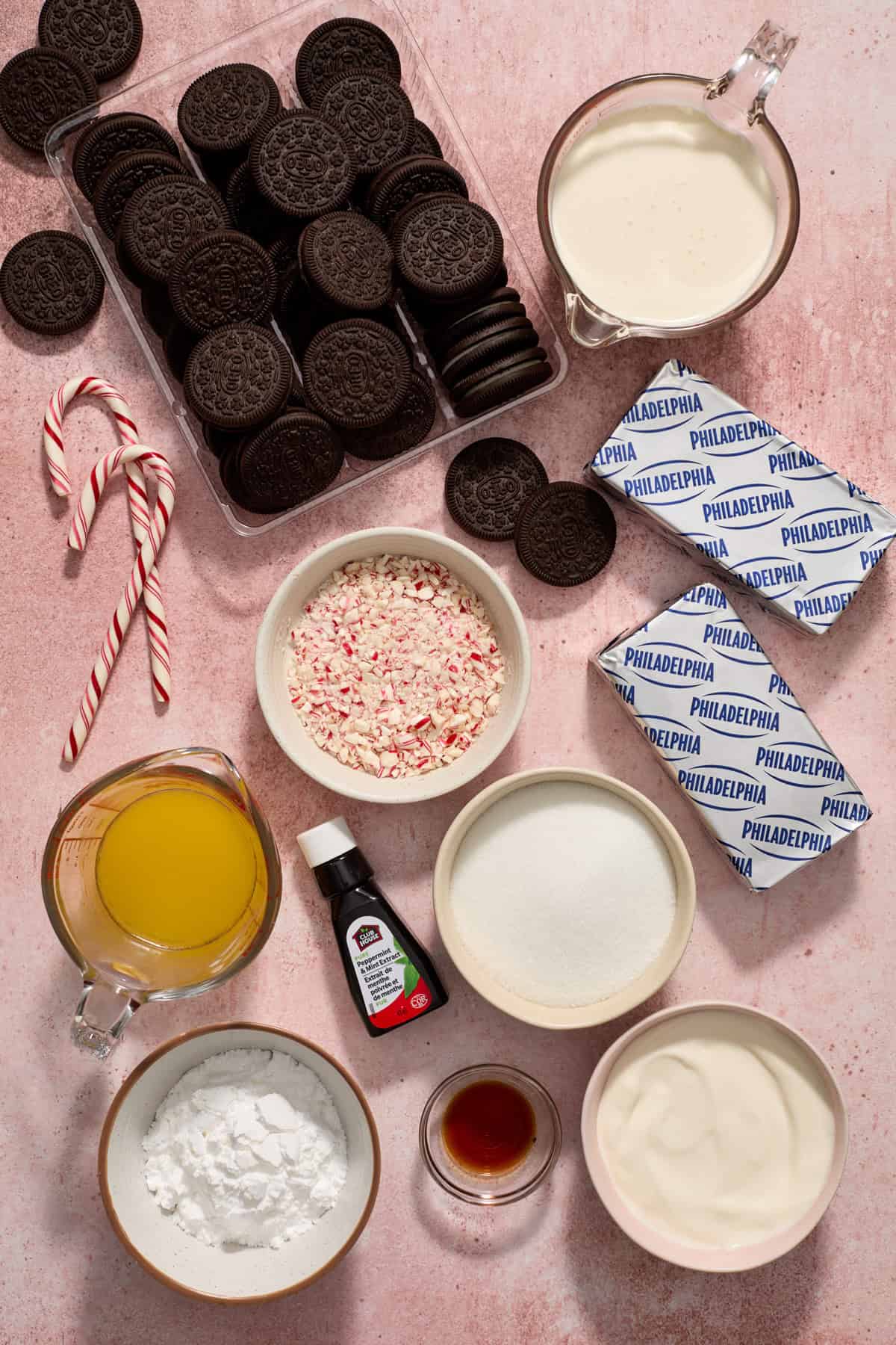 Oreos, cream cheese, peppermint extract, candy canes, cream and other ingredients measured and arranged on surface.