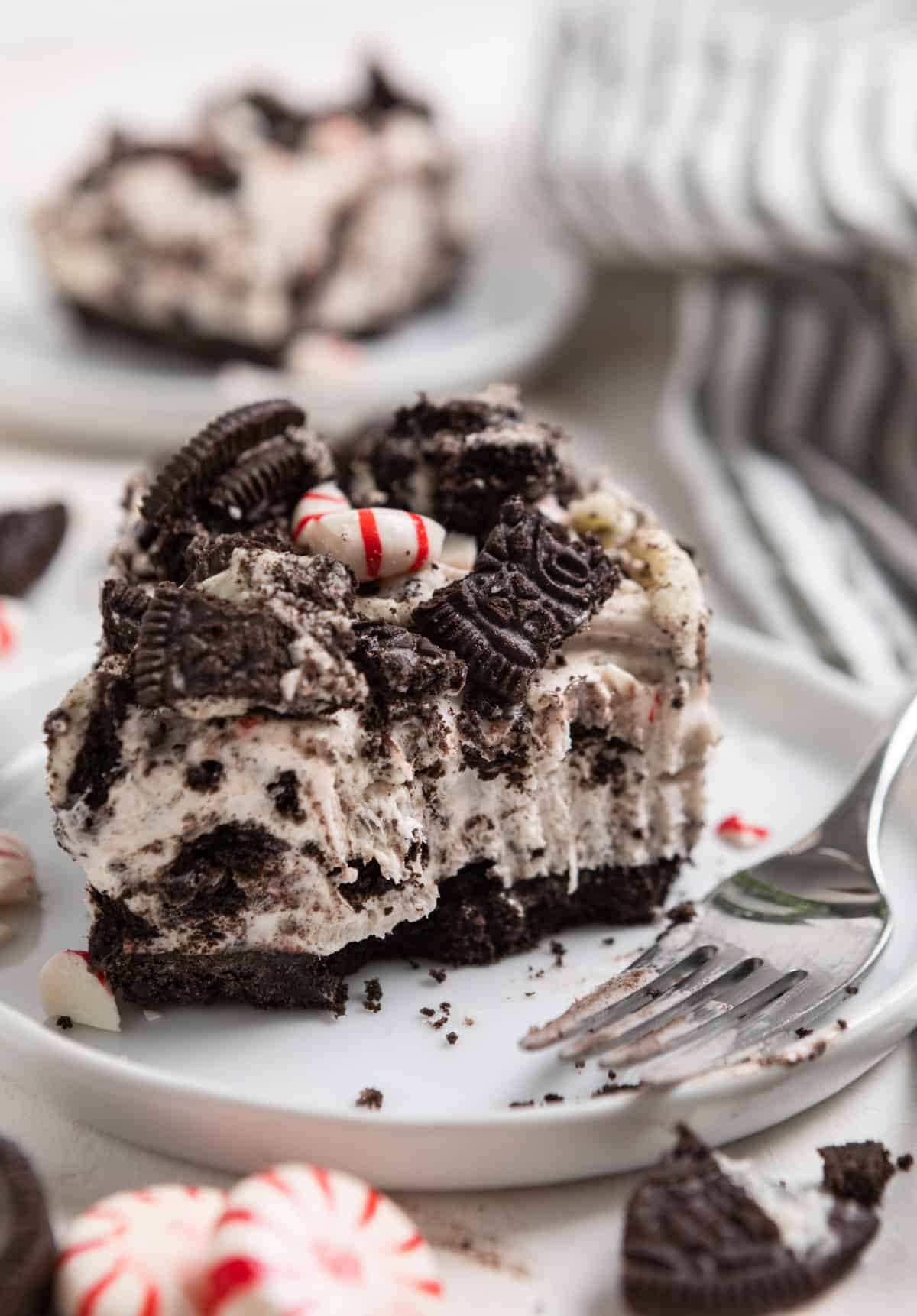 Slice of candy cane cheesecake with oreos on white plate with fork.