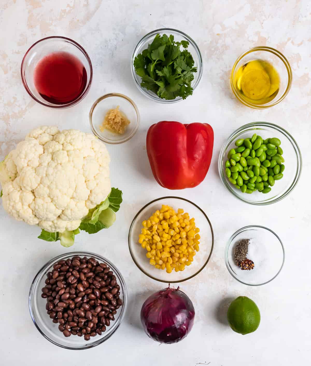 Cauliflower, corn, black beans, peppers, lime and other ingredients on counter.