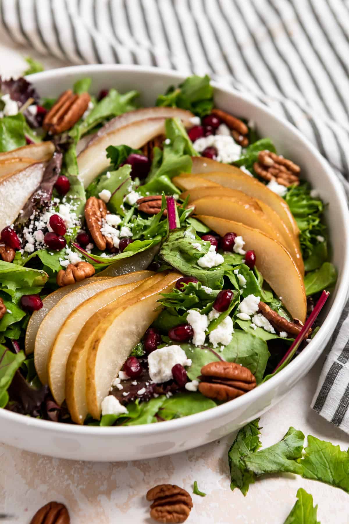 White salad bowl with spring greens, roasted pears, pomegranates, goat cheese and pecans.
