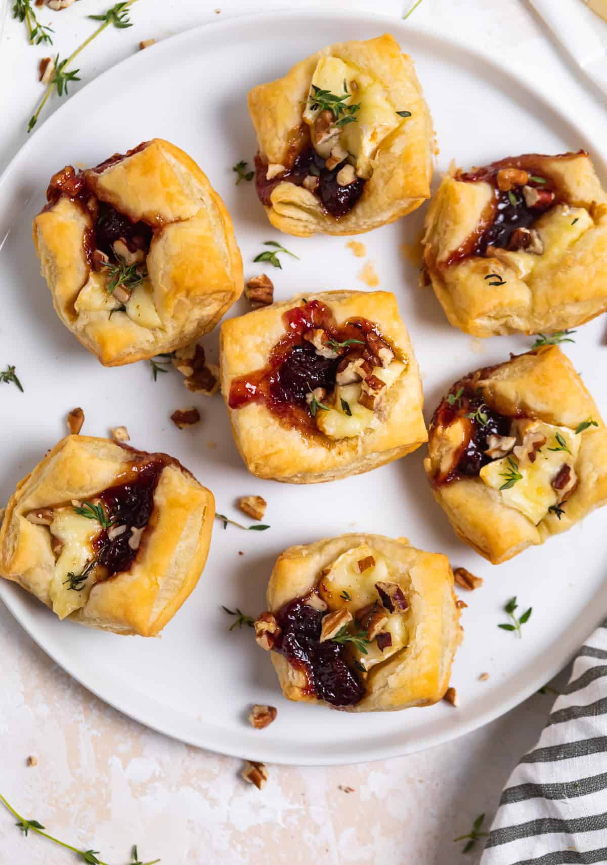 White plate with puff pastry brie bites and thyme surrounding.