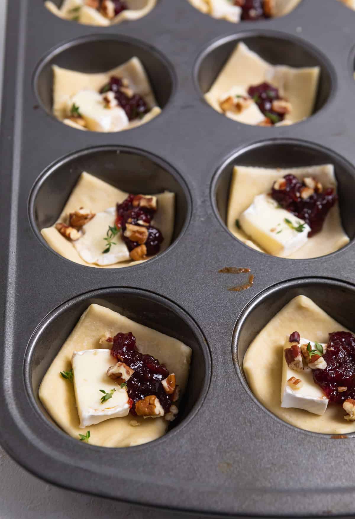 Muffin tin with puff pastry topped with brie, jam, pecans and thyme.