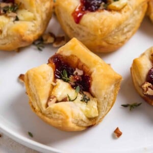 Puff pastry brie bites on white plate with jam and fresh thyme.