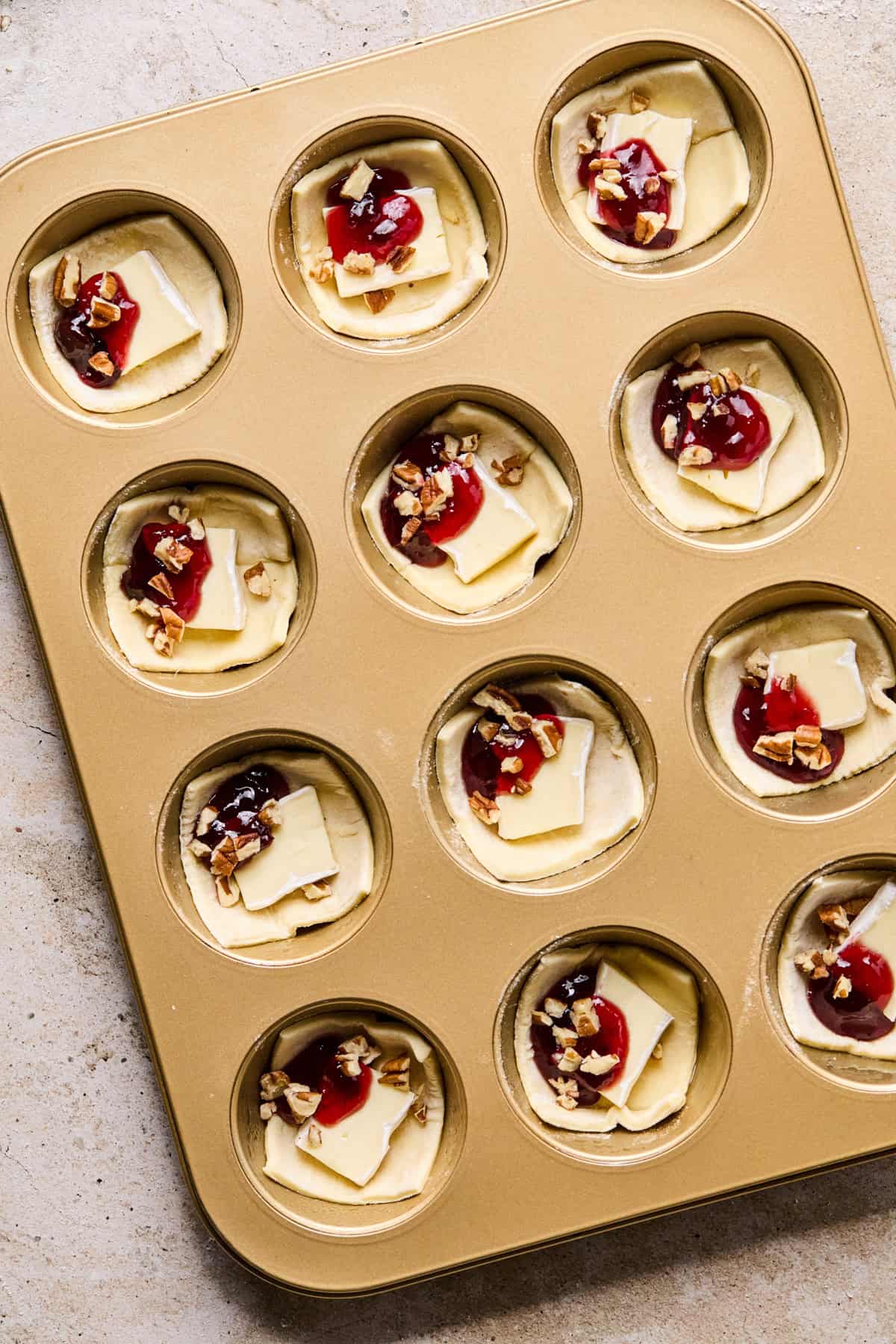 Puff pastry brie bites topped with jam before baking.