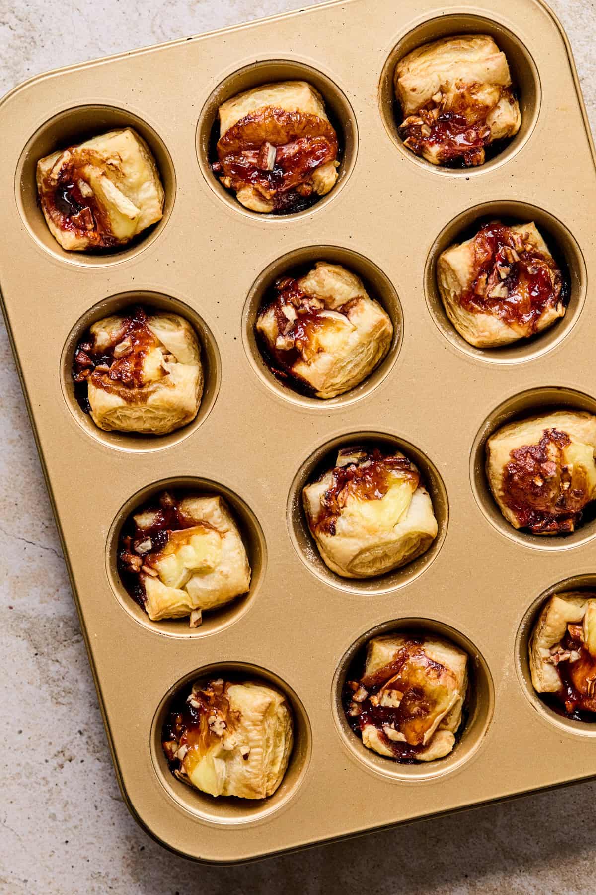 Muffin tin with baked brie bites in puff pastry.