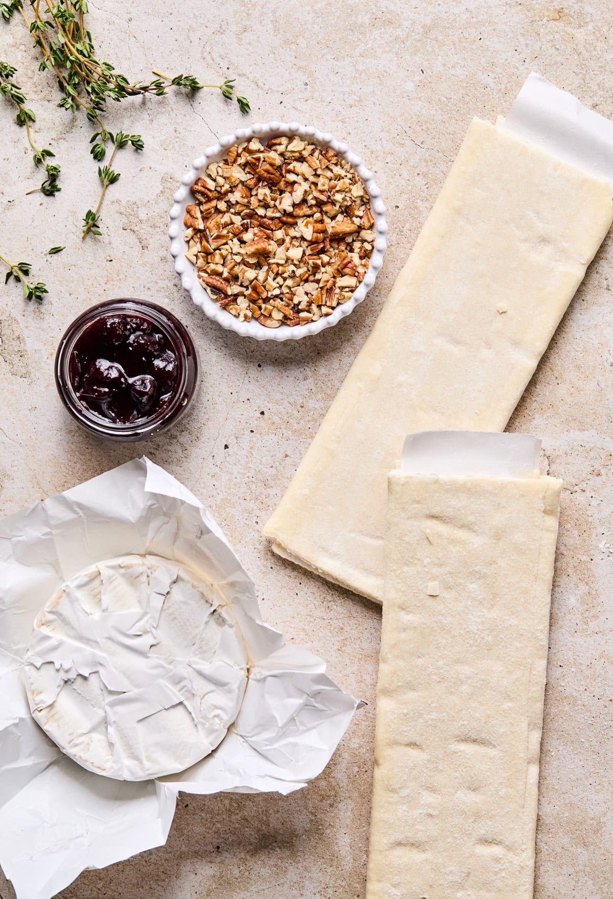 Sheets of puff pastry, brie cheese, preserves, and other ingredients on surface.