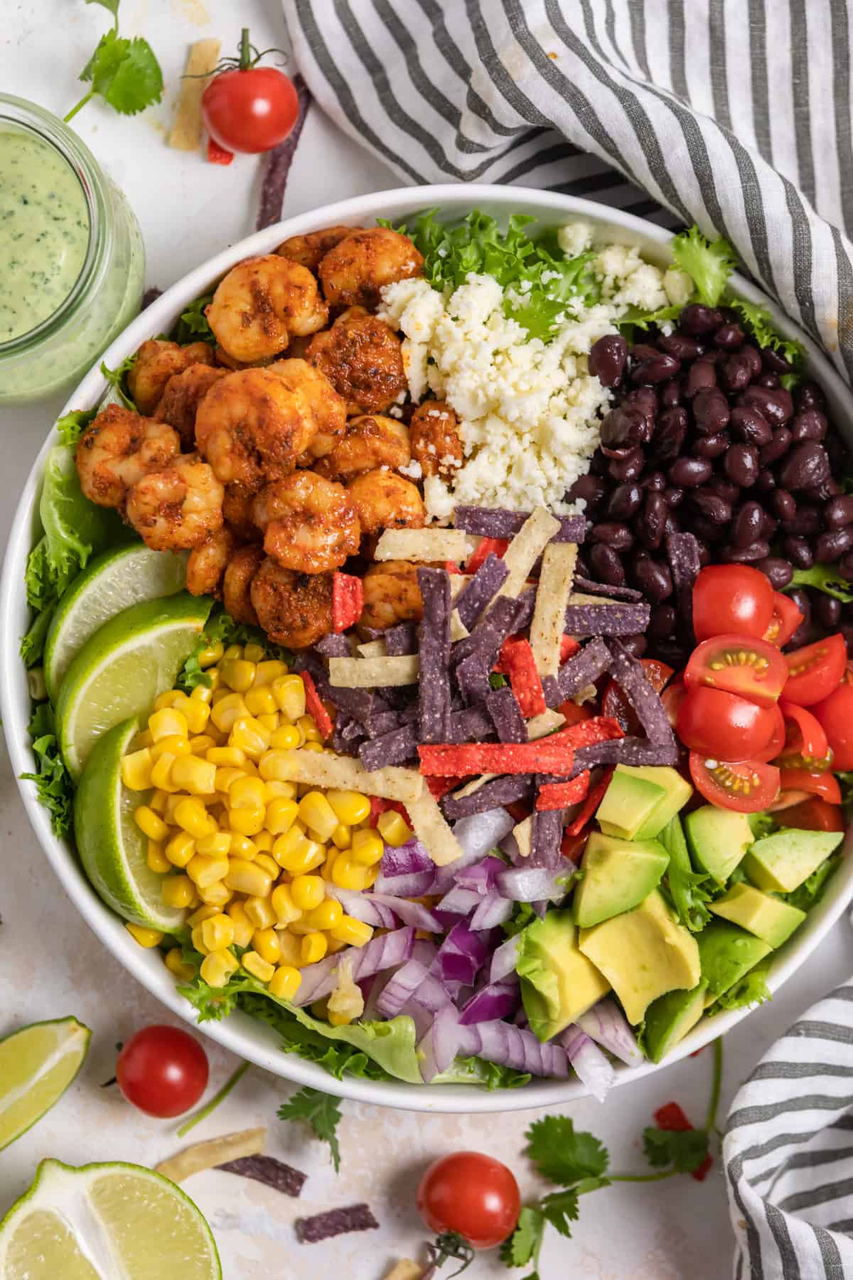 Overhead shot of white bowl with shrimp taco salad with avocado, cheese, black beans etc.