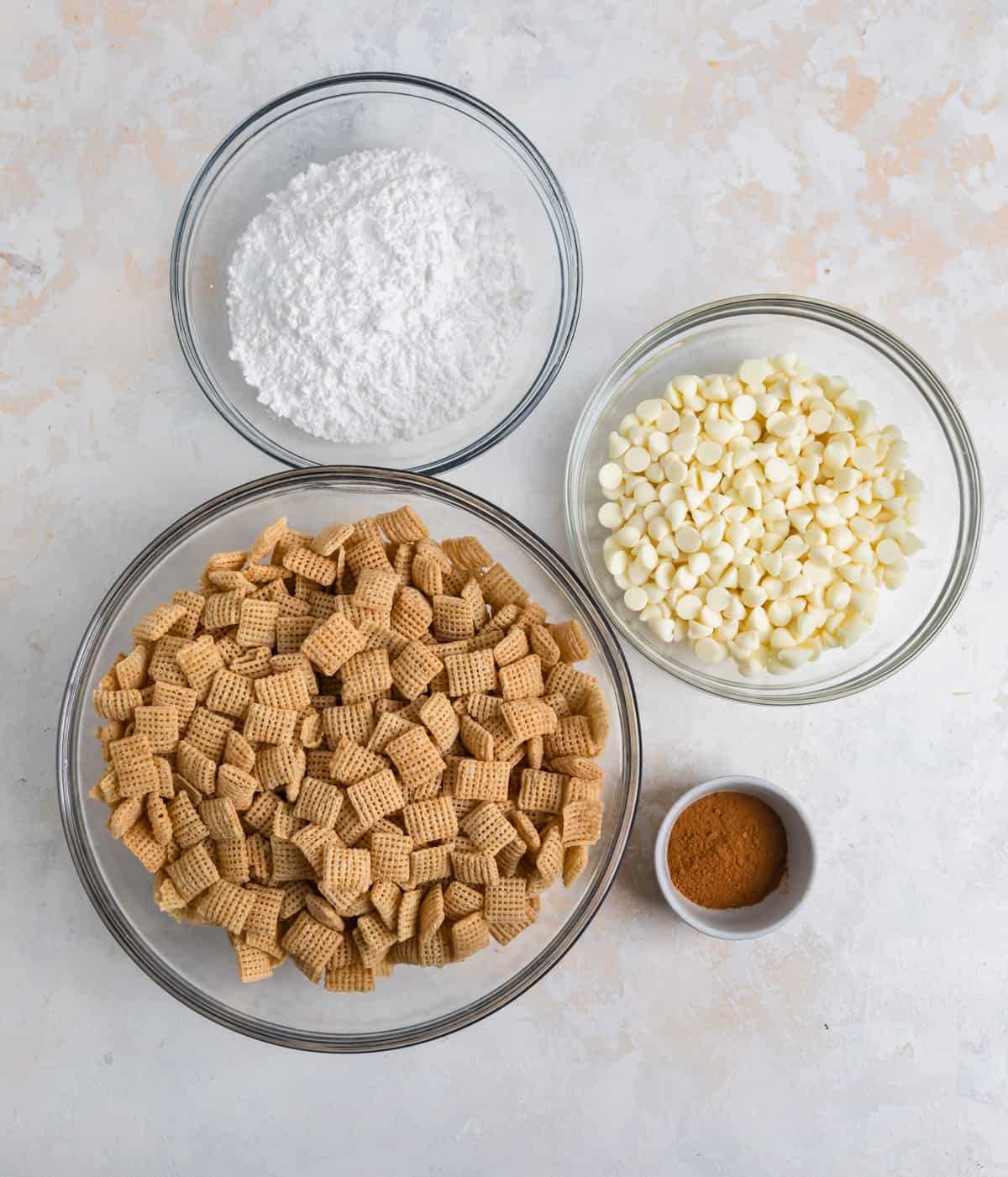 Powdered sugar, white chocolate chips, cinnamon and Chex cereal on counter.
