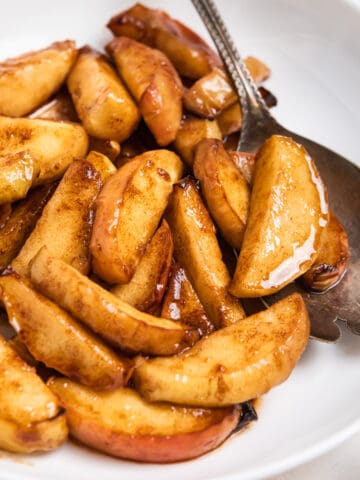 White plate with cinnamon air fryer apples with spoon.