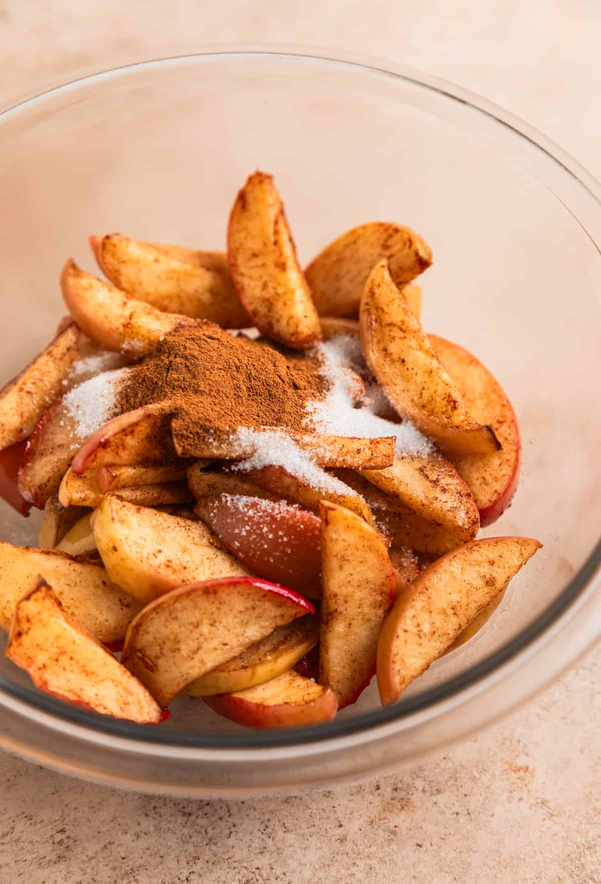 Air fryer cinnamon apples in glass mixing bowl with melted butter, sugar and cinnamon poured on top.
