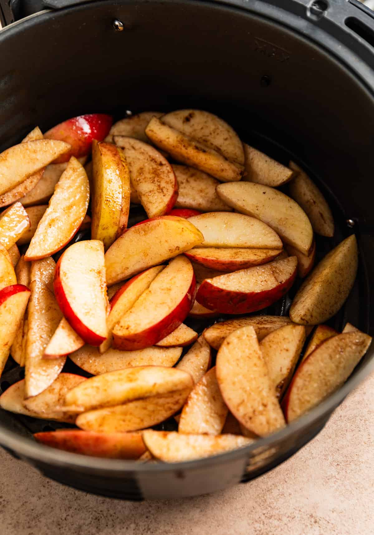 Air fryer basket with sliced apples tossed in oil and cinnamon before cooking.