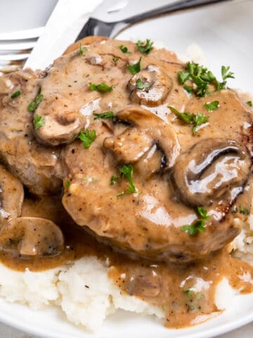 Cream of mushroom bone in pork chop with parsley on top over mashed potatoes.
