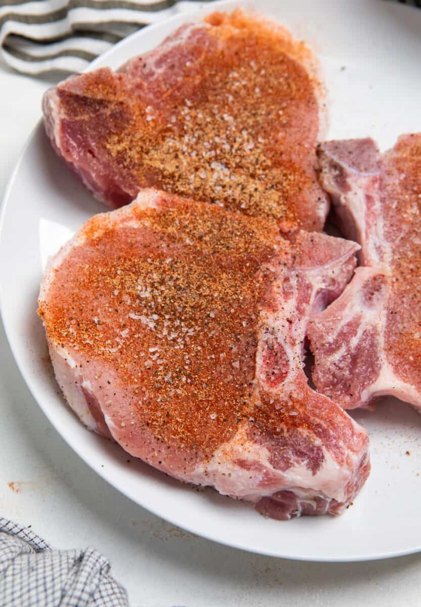 Pork chops with seasoning on white plate.