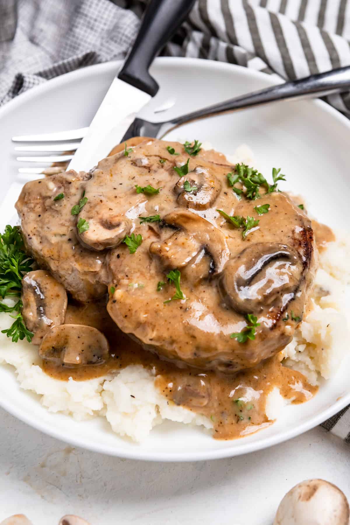 Cream of mushroom pork chop on mashed potatoes with fork and knife.