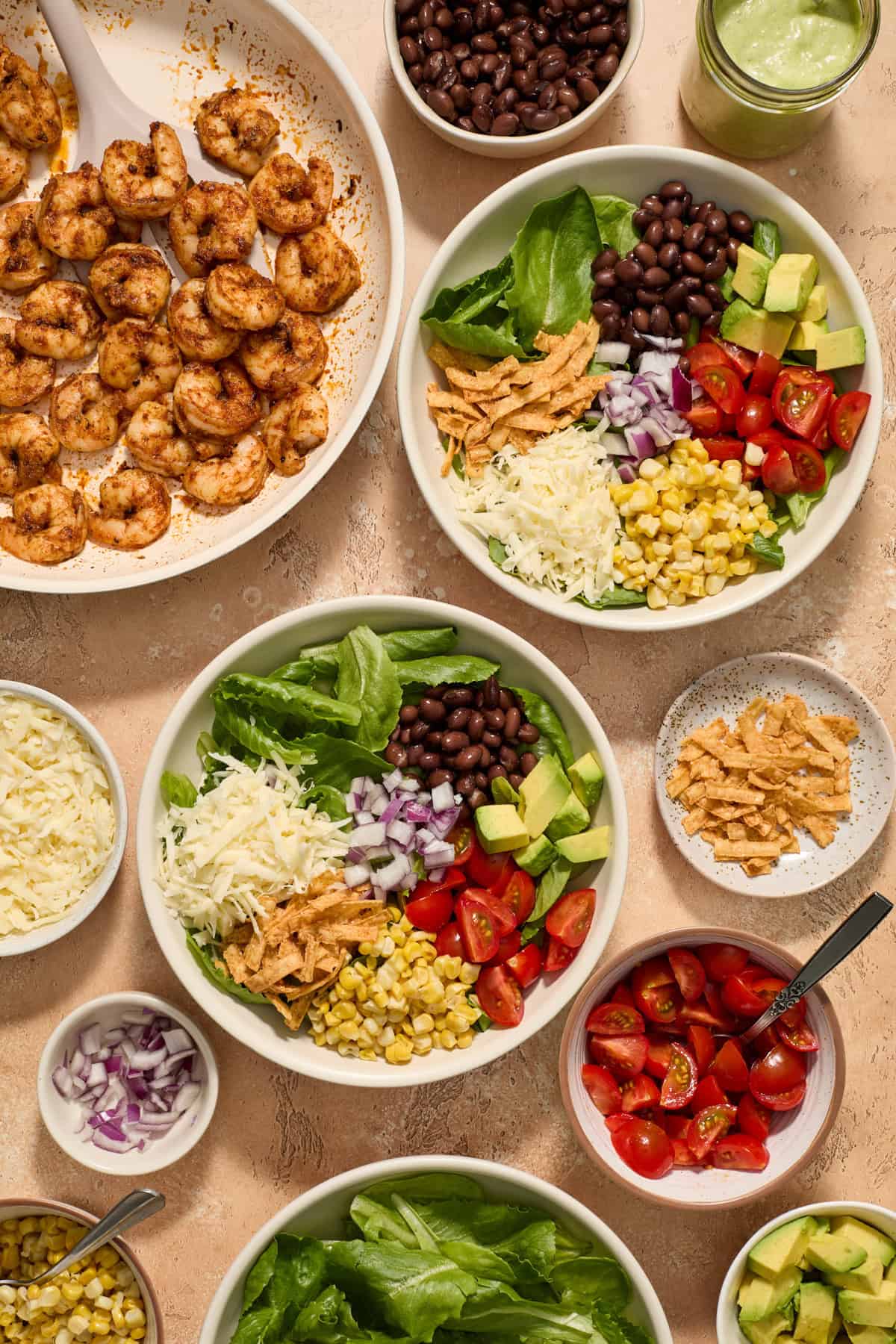 Salad bowls with greens, onion, corn and other ingredients prepared and ready to be topped with cooked shrimp.