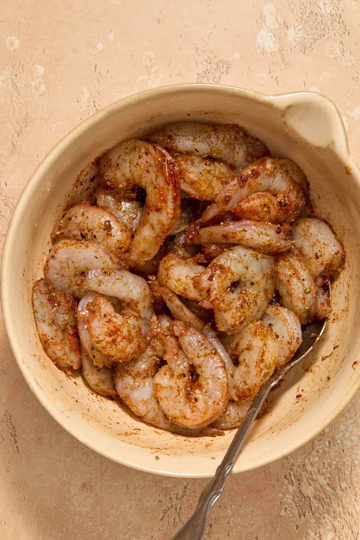 Seasoned shrimp in mixing bowl with spoon.