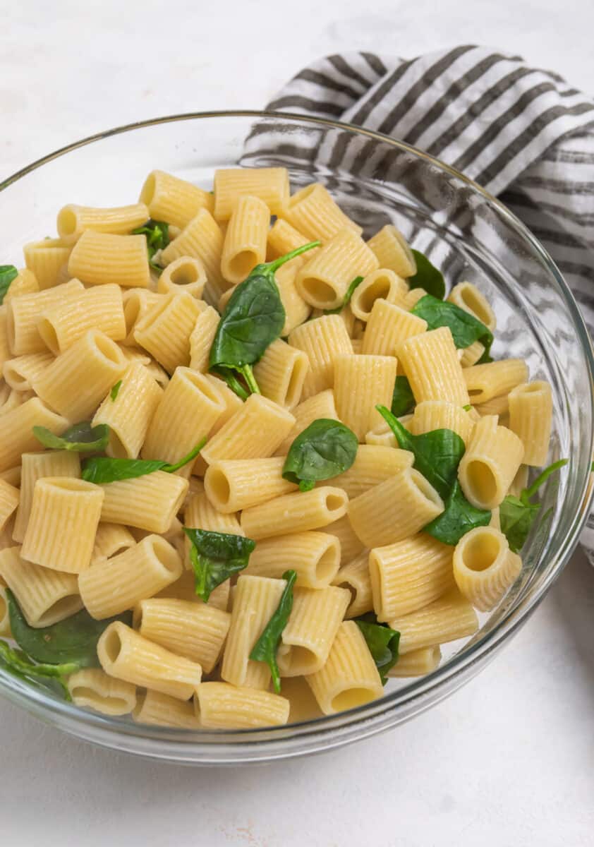 Glass bowl with rigatoni and spinach in it.
