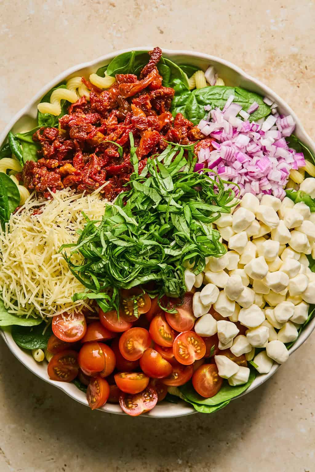 Pasta in bowl topped with mozzarella pearls, onions, shredded parmesan and other ingredients.